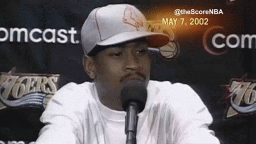 A Man Wearing A Hat Is Speaking Into A Microphone . GIF