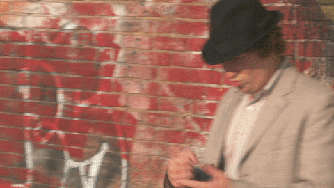 A Man Wearing A Hat Is Standing In Front Of A Brick Wall GIF