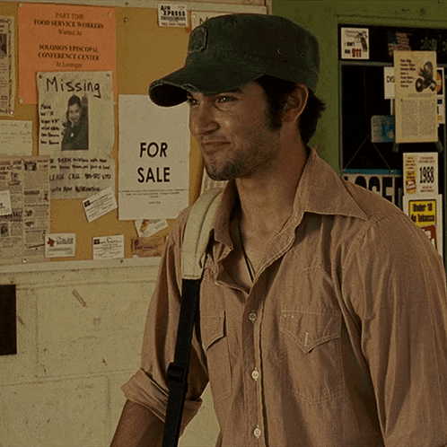 A Man Wearing A Hat Is Standing In Front Of A Bulletin Board With Missing And For Sale Signs On It GIF