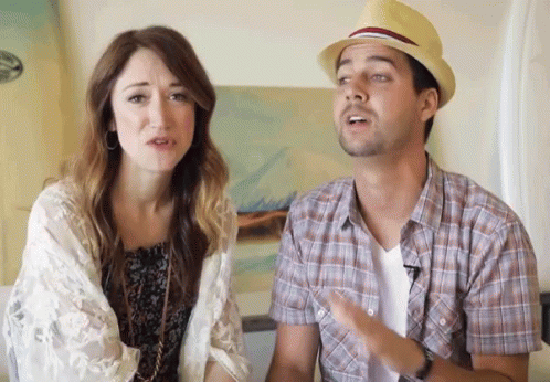 A Man Wearing A Hat Is Talking To A Woman Who Is Looking At Him GIF