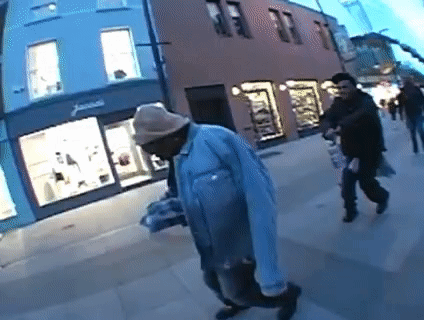 A Man Wearing A Hat Is Walking Down A Sidewalk In Front Of A Store That Says James GIF