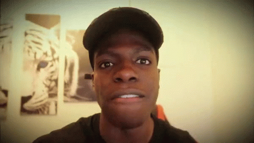 A Man Wearing A Hat Looks At The Camera With A Picture Of A Tiger In The Background GIF