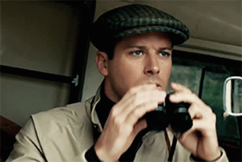 A Man Wearing A Hat Looks Through Binoculars In A Car GIF