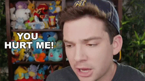 A Man Wearing A Hat Says " You Hurt Me " In Front Of A Shelf Full Of Stuffed Animals GIF