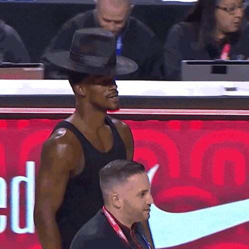 A Man Wearing A Hat Stands In Front Of A Red Nike Sign GIF