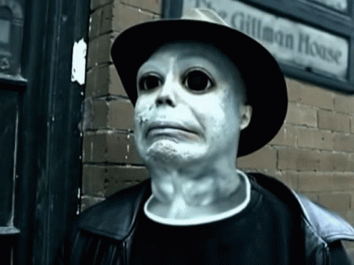 A Man Wearing A Hat Stands In Front Of A Sign That Says Gilman House GIF