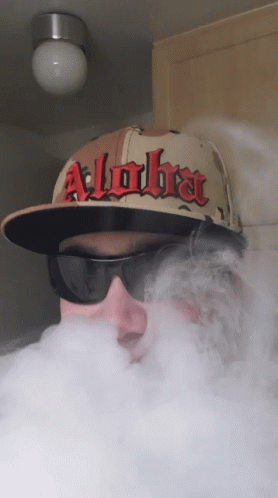 A Man Wearing A Hat That Says Alpha Is Blowing Smoke GIF