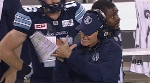 A Man Wearing A Hat That Says Argonauts Talks To A Football Player GIF