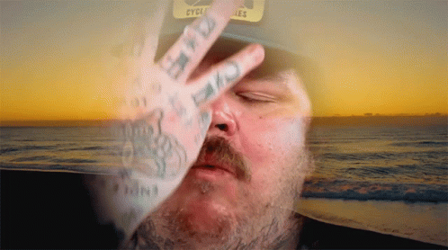 A Man Wearing A Hat That Says Cycles Covers His Face With His Hand GIF