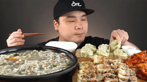 a man wearing a hat that says dnt is eating noodles and meat