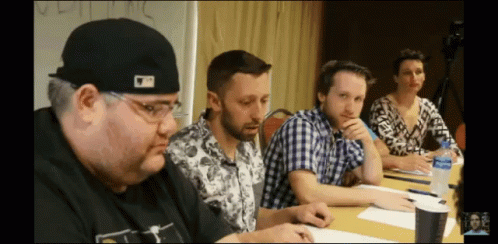 A Man Wearing A Hat That Says ' Mlb ' On It Sits At A Table GIF