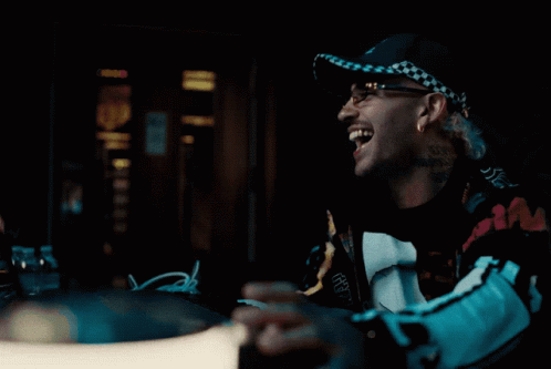 A Man Wearing A Hat With A Checkered Pattern Is Laughing And Holding A Bottle GIF