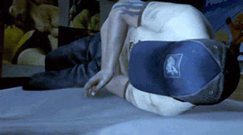 A Man Wearing A Hat With The Letter A On It Is Laying On A Bed GIF