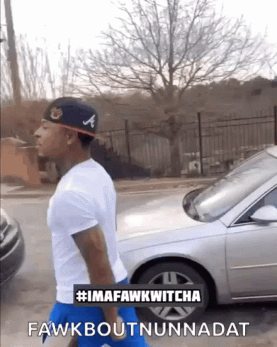 A Man Wearing A Hat With The Letter A On It Is Walking Down A Street GIF