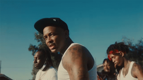 A Man Wearing A Hat With The Letter T On It Stands In Front Of A Group Of Men GIF