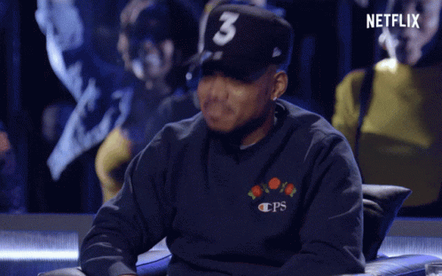 A Man Wearing A Hat With The Number 3 On It Sits In A Chair GIF