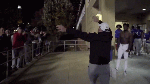 A Man Wearing A Hat With The Number 33 On It Stands In Front Of A Crowd Of People GIF