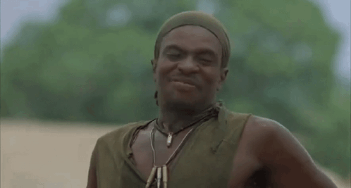 A Man Wearing A Head Scarf And A Necklace Is Standing In The Dirt . GIF