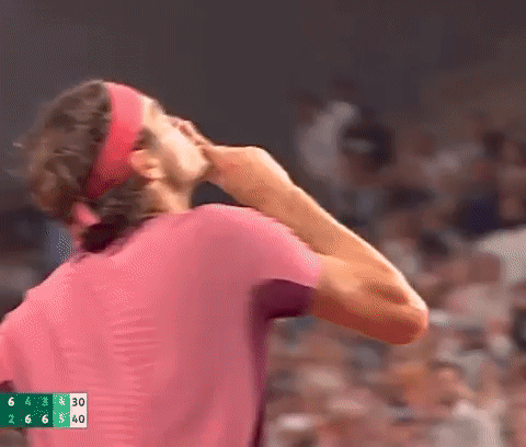 A Man Wearing A Headband And A Pink Shirt Is Standing In Front Of A Crowd And Covering His Face With His Hand . GIF