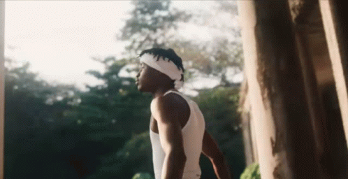A Man Wearing A Headband And A Tank Top Is Standing In Front Of A Tree . GIF