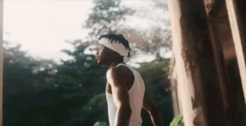 A Man Wearing A Headband And A White Tank Top Is Standing In Front Of A Tree . GIF