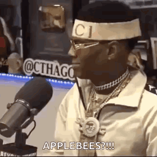 A Man Wearing A Headband And Glasses Is Standing In Front Of A Microphone . GIF