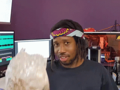 A Man Wearing A Headband Holds A Bag Of Popcorn In Front Of A Purple Wall GIF