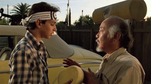 A Man Wearing A Headband With A C On It Talks To Another Man GIF