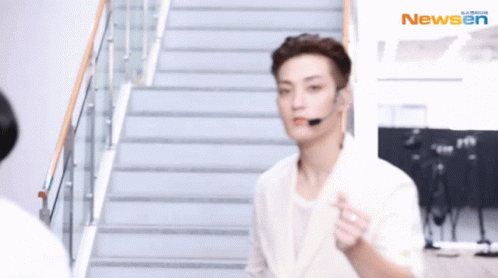 A Man Wearing A Headset Is Walking Down A Set Of Stairs With The Newsen Logo In The Background GIF