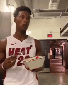 A Man Wearing A Heat Jersey Is Holding A Box Of Food GIF