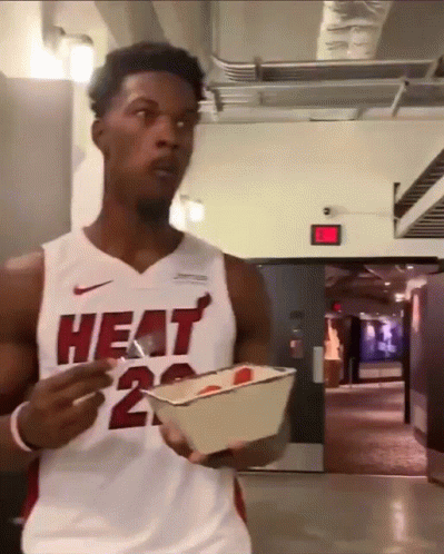 A Man Wearing A Heat Jersey Is Holding A Container Of Food GIF