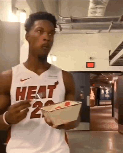 A Man Wearing A Heat Jersey Is Holding A Container Of Food GIF