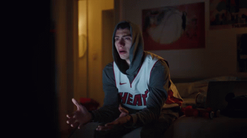 A Man Wearing A Heat Jersey Sits On A Bed At Night GIF
