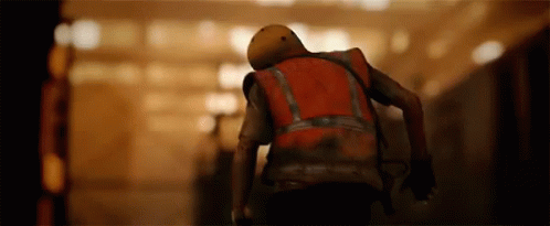 A Man Wearing A Helmet And A Red Vest Is Walking Down A Hallway . GIF