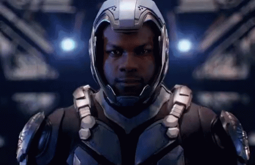A Man Wearing A Helmet And Armor Is Standing In A Dark Room . GIF