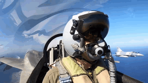 A Man Wearing A Helmet And Goggles Is Flying A Fighter Jet Over The Ocean GIF