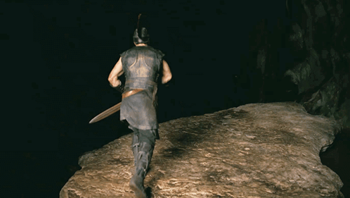 A Man Wearing A Helmet And Holding A Sword Is Walking On A Rock In The Dark GIF