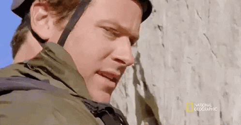A Man Wearing A Helmet And Jacket Is Standing Next To A Rock Wall . GIF