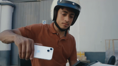 A Man Wearing A Helmet Holds A White Iphone GIF