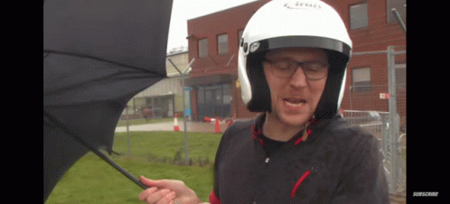 A Man Wearing A Helmet Is Holding An Umbrella In Front Of A Building GIF