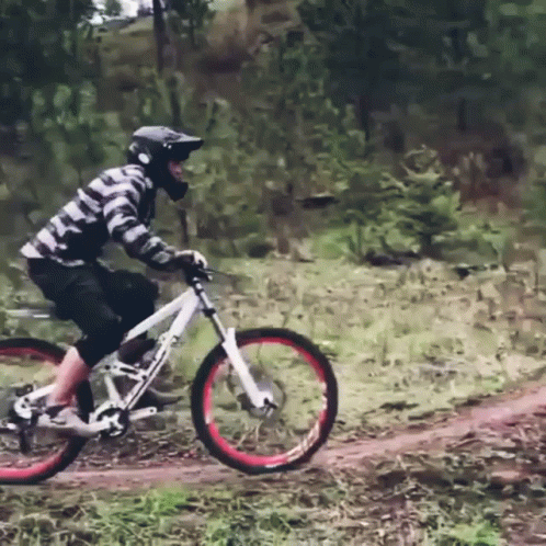 A Man Wearing A Helmet Is Riding A Bike On A Dirt Path GIF