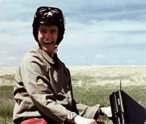 A Man Wearing A Helmet Is Sitting In A Field Holding A Briefcase With The Letter P On It GIF