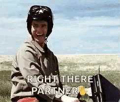 A Man Wearing A Helmet Is Sitting In A Field With A Laptop And A Sign That Says Right There Partner . GIF