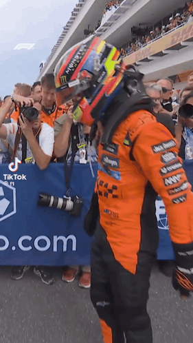 A Man Wearing A Helmet Is Standing In Front Of A Crowd Of People At A Race Track . GIF