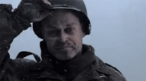 A Man Wearing A Helmet Is Standing In The Snow And Looking At The Camera . GIF
