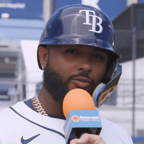 A Man Wearing A Helmet With The Letter Tb On It Holds An Orange Microphone GIF