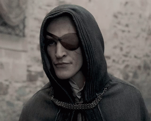 A Man Wearing A Hooded Cape And An Eye Patch Looks At The Camera GIF