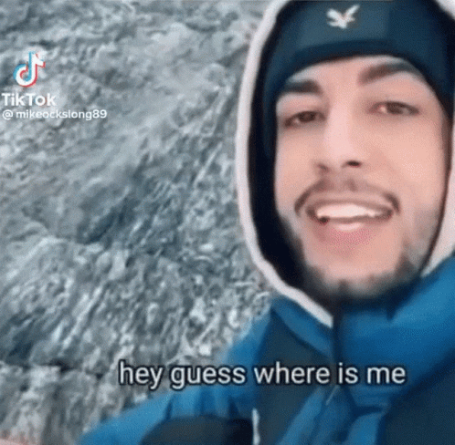 A Man Wearing A Hooded Jacket And A Beanie Is Smiling And Says Hey Guess Where Is Me GIF