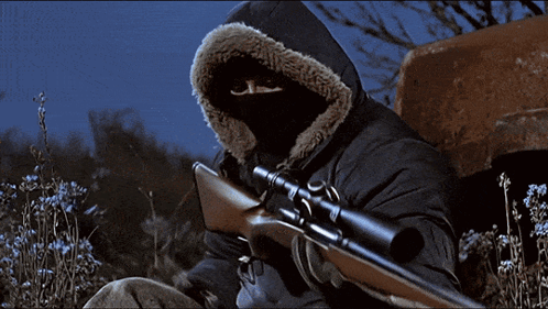 A Man Wearing A Hooded Jacket Is Holding A Sniper Rifle GIF