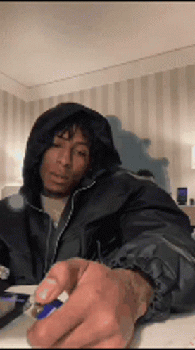 A Man Wearing A Hooded Jacket Is Sitting At A Table Holding A Lighter . GIF